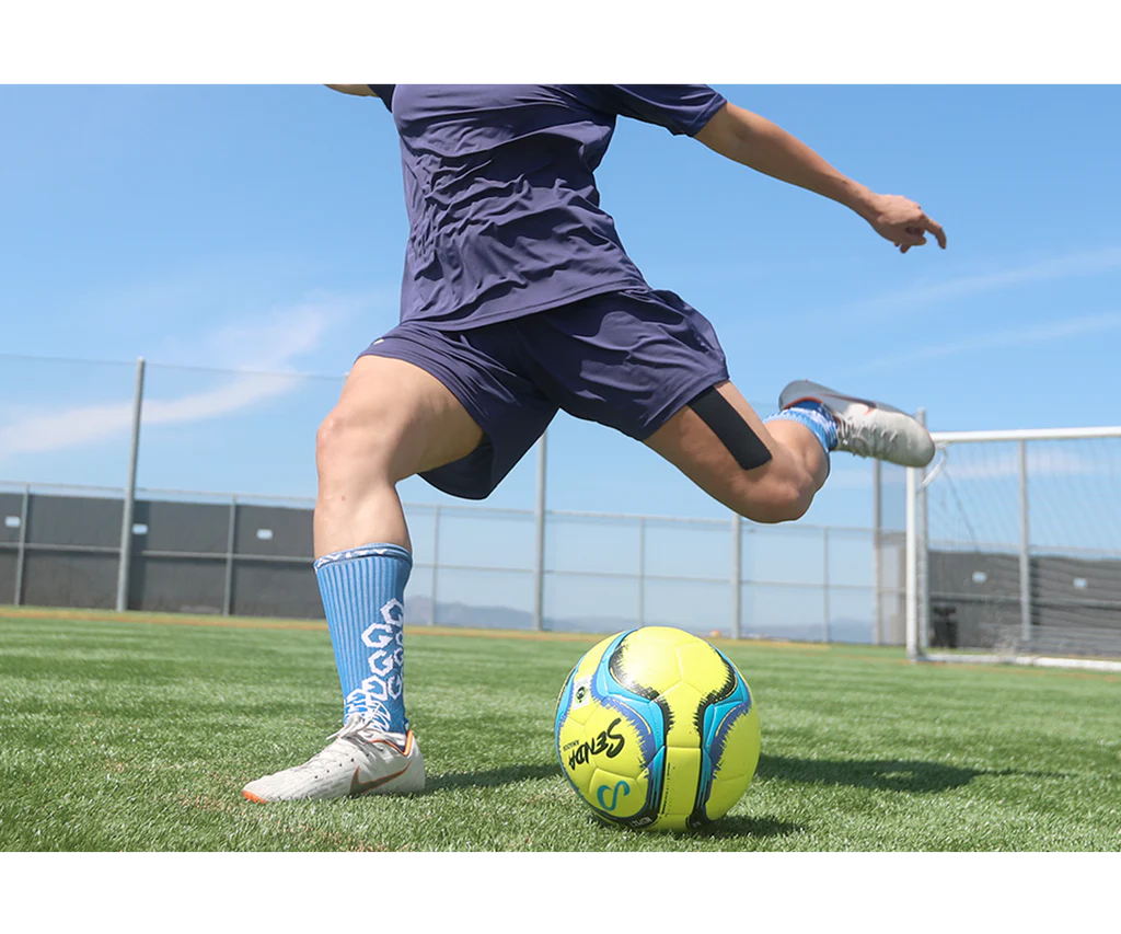 Athlete in motion kicking Senda Amador Training Soccer Ball in yellow on outdoor turf, showcasing real-play performance and vibrant design.