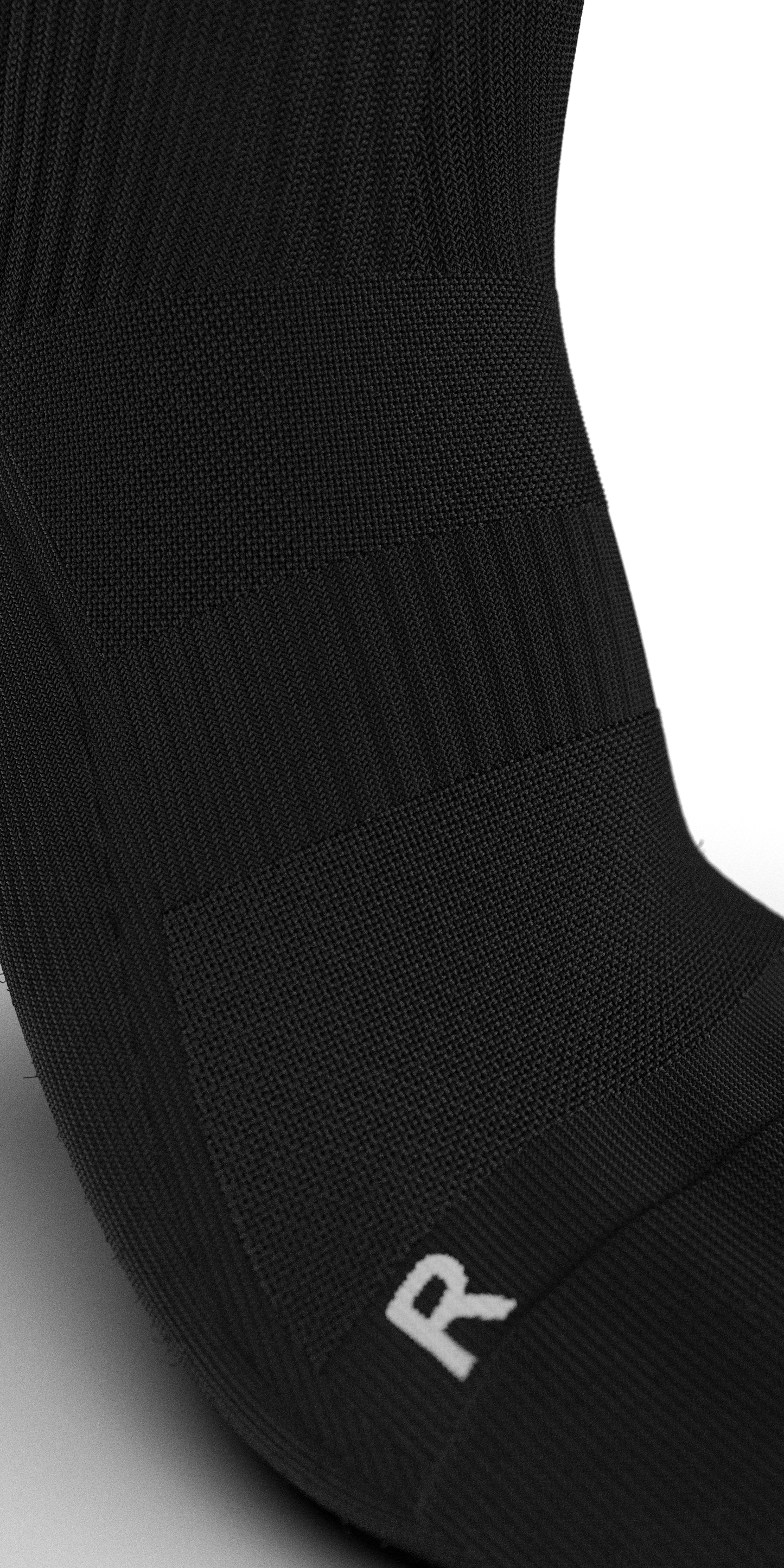 Extreme close-up of the Senda Gravity Pro Grip Sock in black, highlighting ribbed compression bands and 'R' marking for right-foot ergonomic fit.