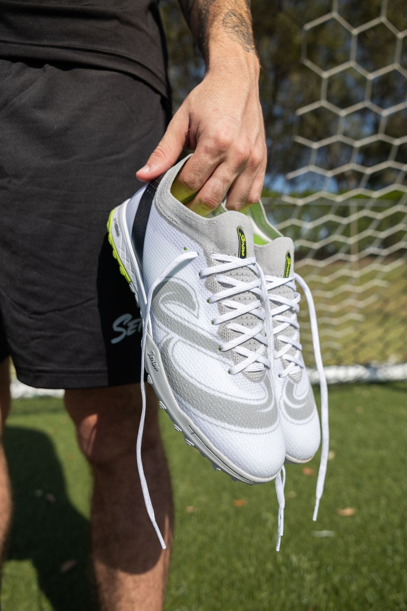 Close-up of Senda Pampa Pro Turf Cleats held by player on soccer field, showcasing sleek design, breathable upper, and textured sole grip.