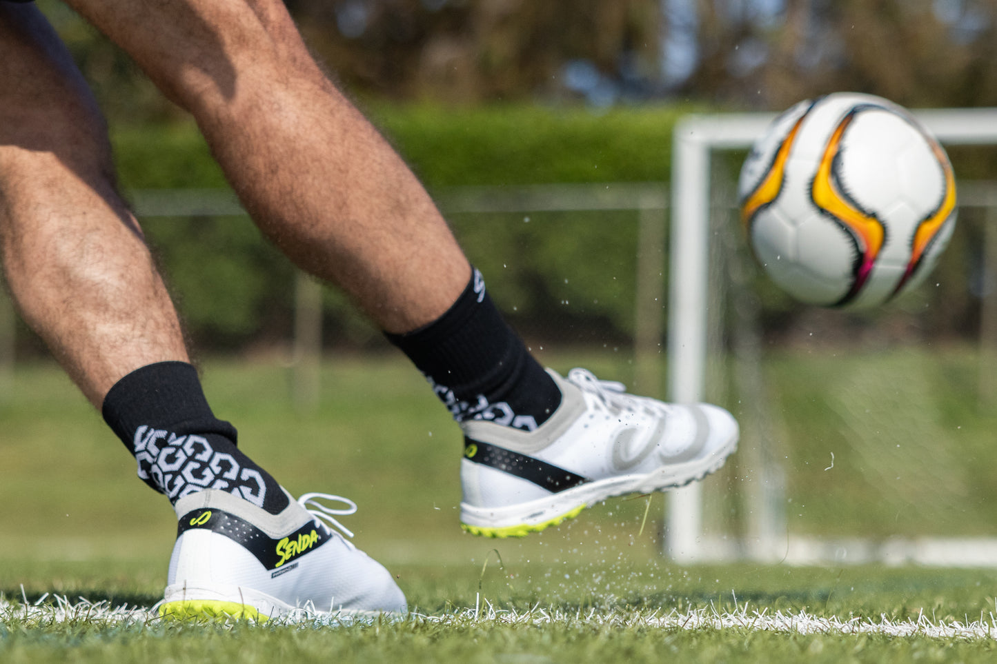 Player wearing Senda Pampa Pro Turf Cleats kicks soccer ball on grass field, highlighting sole grip and dynamic performance design.
