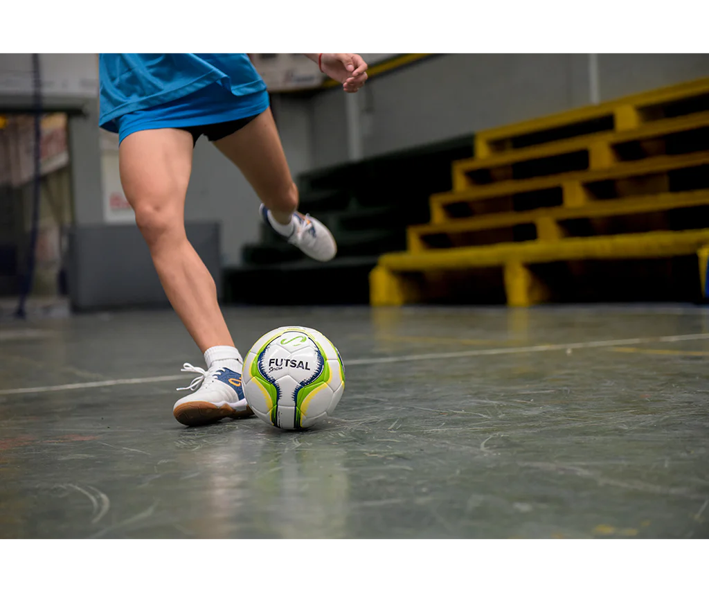 Futsal player dribbling Senda Rio Match Futsal ball in green on a polished indoor court.