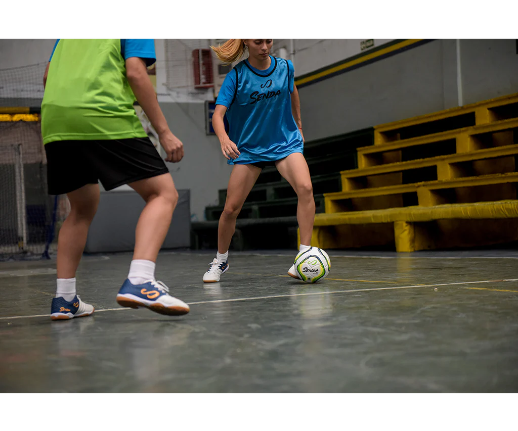 Female futsal player wearing Senda gear dribbles the Rio Match Futsal ball on an indoor hard court.