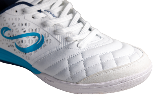 Close-up of white Ushuaia Club 2.0 futsal shoe by Senda, showing textured synthetic leather toe box with reinforced stitching and breathable mesh side panels.

