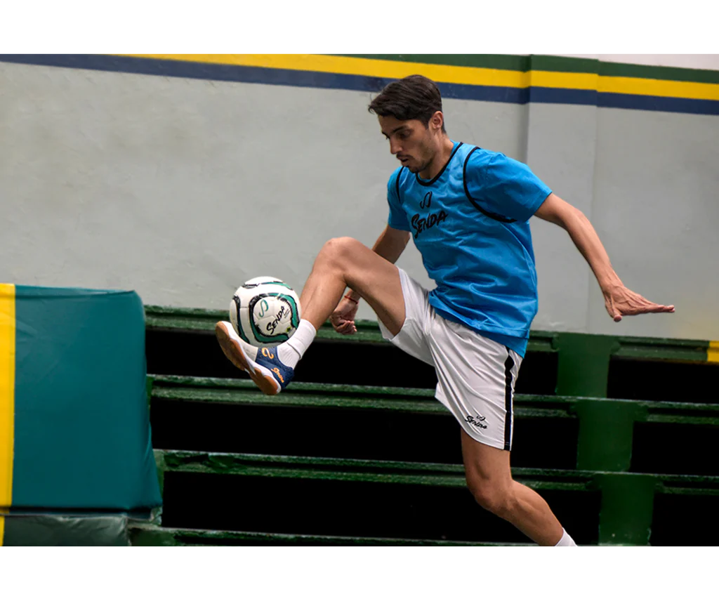 Futsal player juggling the Senda Bahia Ball mid-air during an indoor freestyle trick session, showcasing ball control and responsiveness.

