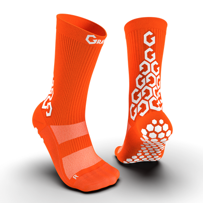 Vibrant orange Senda Gravity Pro Crew Socks with anti-slip white grip pads and geometric logo detailing front and back.

