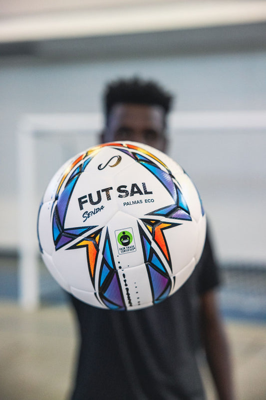 Person holding Senda Palmas Eco Futsal Ball with Fair Trade Certified label and bold geometric pattern clearly visible.


