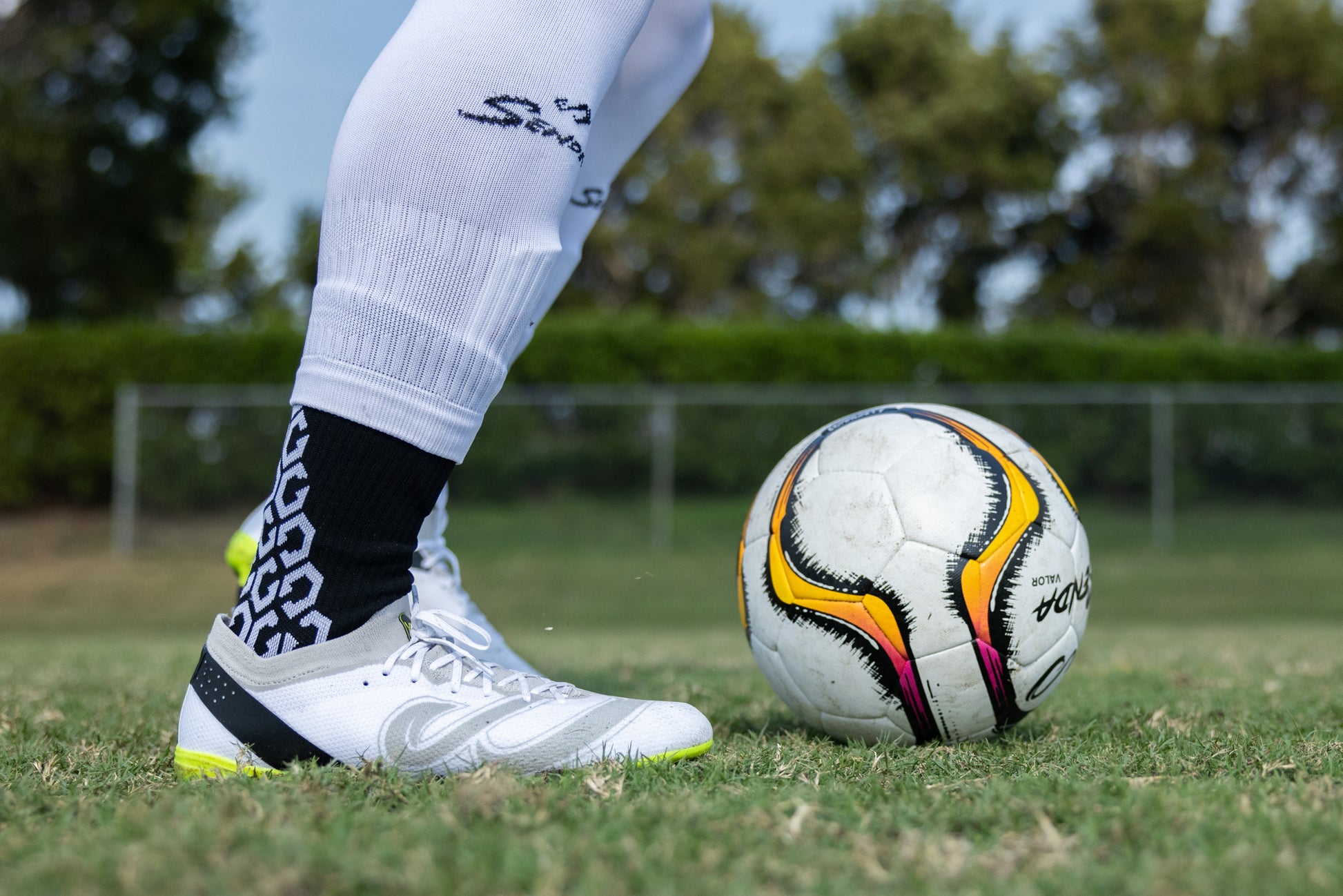 Player wearing Senda Pampa Pro Soccer Cleats controls a ball on grass field with focus on cleat design and ankle support.


