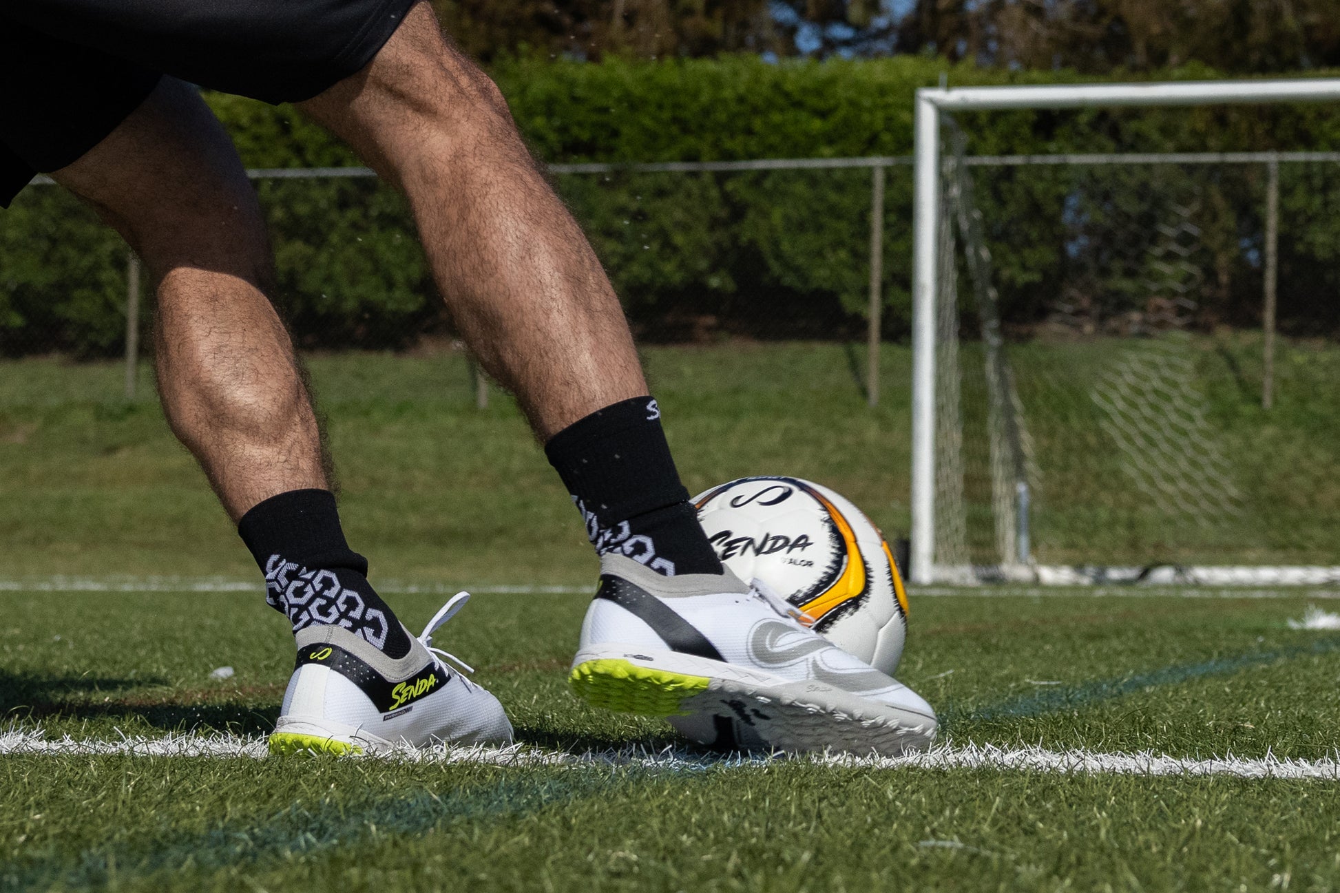 Close-up of athlete dribbling with Senda Pampa Pro Turf Cleats on grass, showing grip sole and sleek low-profile design.

