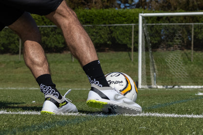 Close-up of athlete dribbling with Senda Pampa Pro Turf Cleats on grass, showing grip sole and sleek low-profile design.

