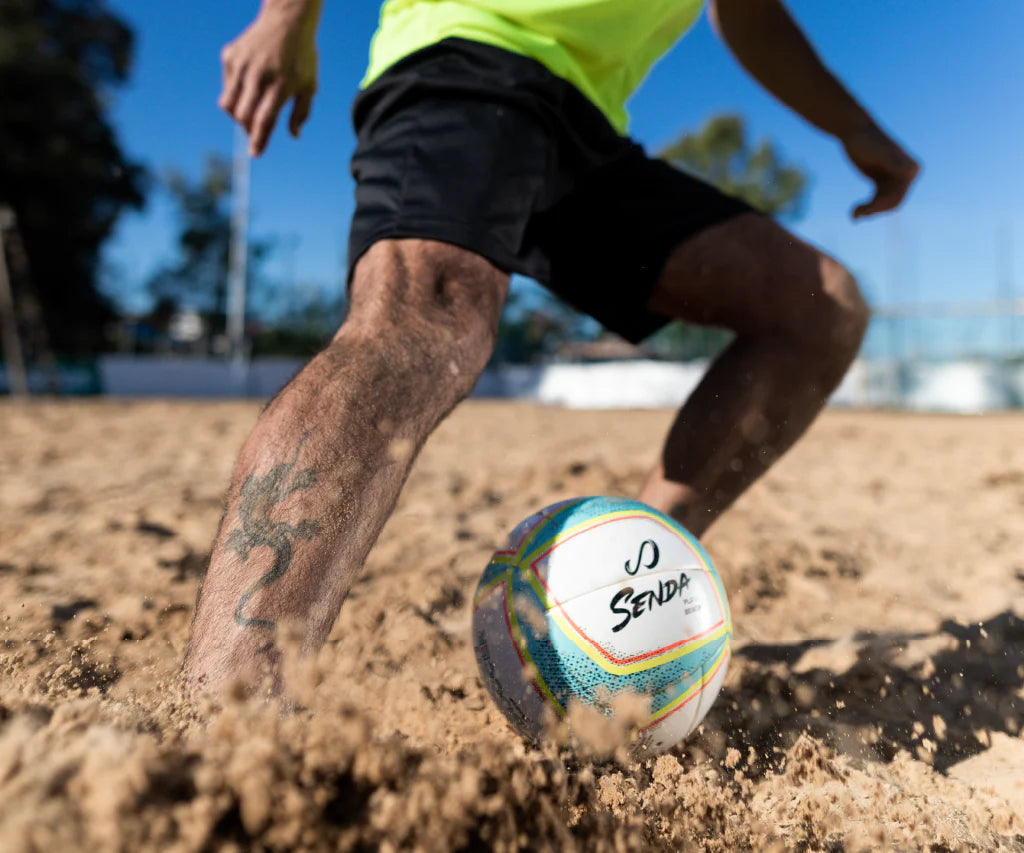 Close-up of athlete controlling the Senda Playa Beach Soccer Ball on sand during a beach soccer match.

