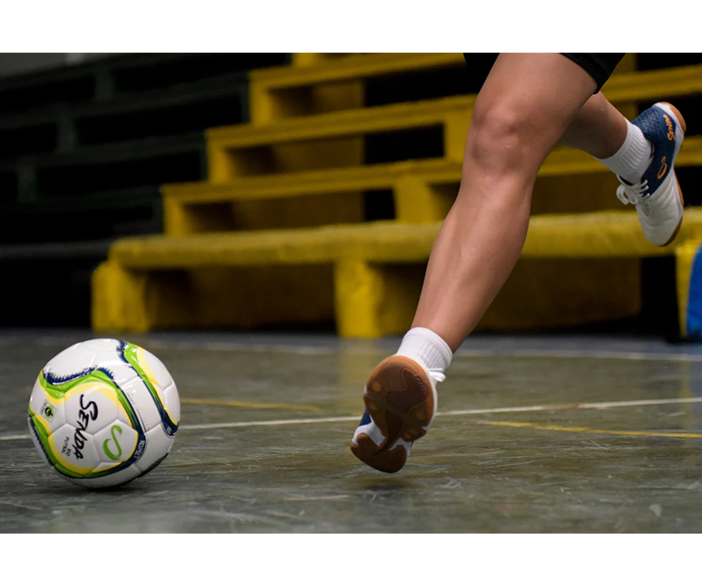 Close-up of player striking the Senda Rio Match Futsal ball on an indoor surface during a game.

