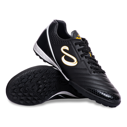 Pair of Senda Ushuaia Academy Turf Black shoes displayed with sole and side view showing grip pattern and bold S logo.

