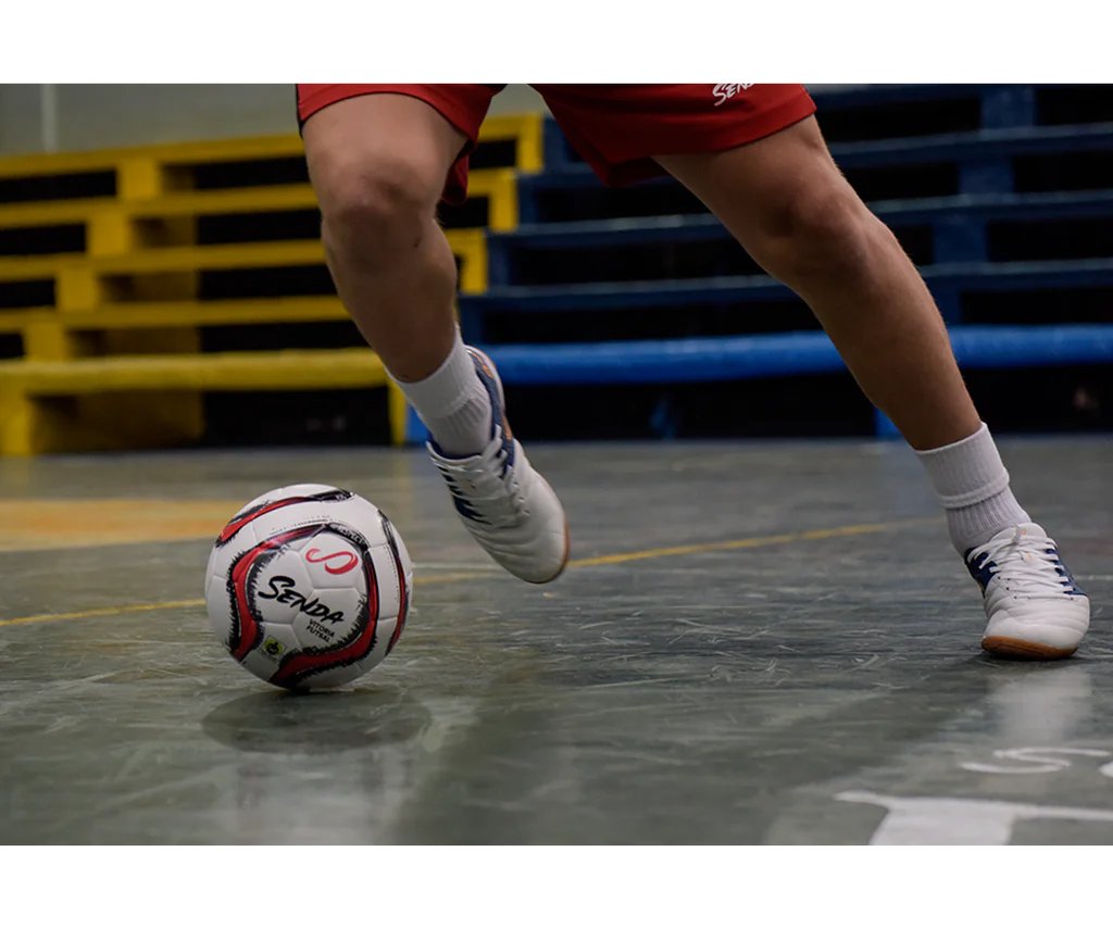 Close-up of player dribbling with Senda Vitoria Premium Match Futsal Ball on indoor court, highlighting grip, texture, and agile footwork.

